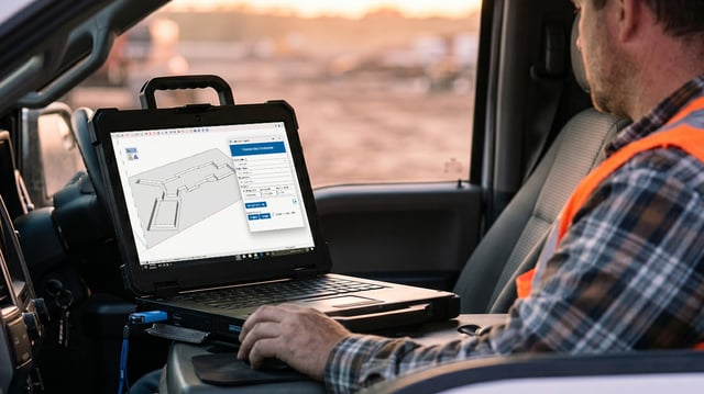 A site contractor in a hi-vis vest working on a Trimble Site Contractor excavation model on a rugged laptop in his truck cab