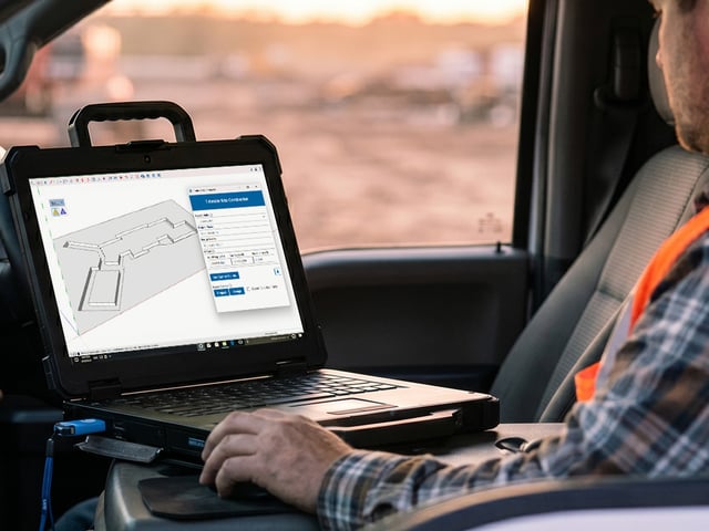 A site contractor working on a Trimble Site Contractor excavation model on a rugged laptop in his truck cab