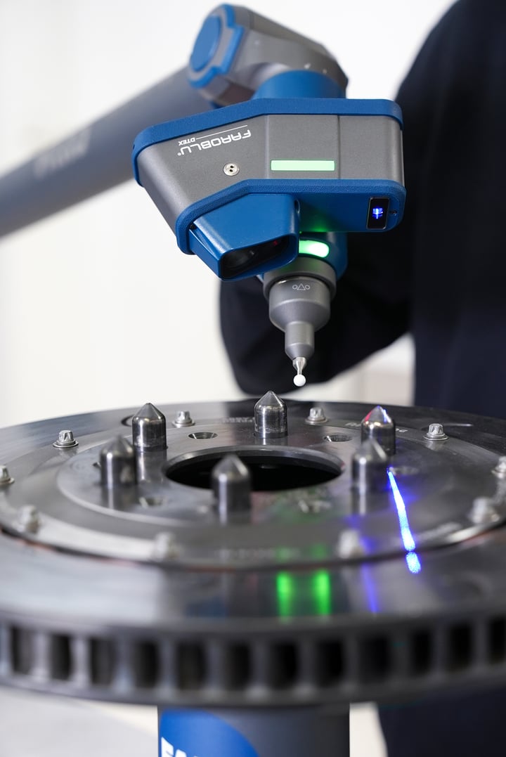 FARO laser line probe on a Quantum X arm scanning a brake rotor, its blue laser line visible on the metal