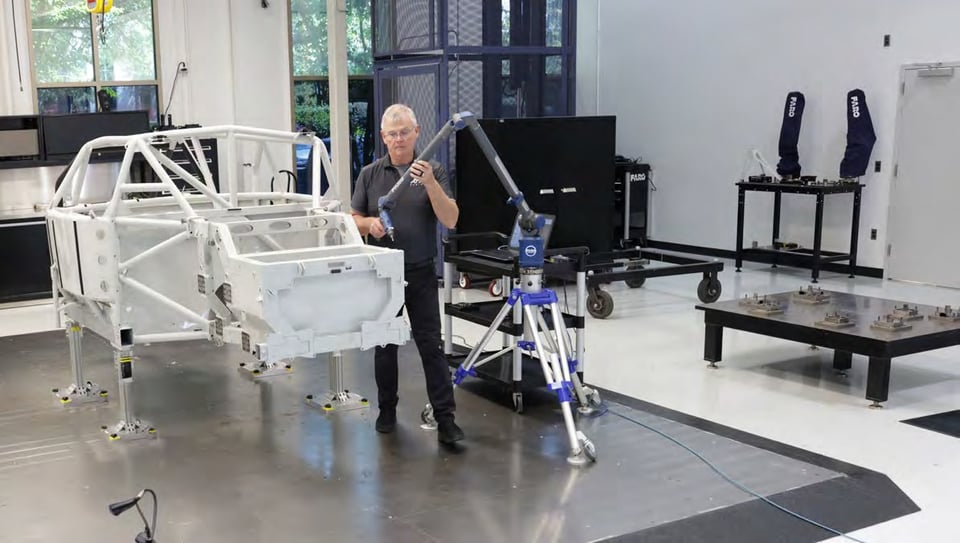 Engineer measuring a white vehicle chassis frame with a FARO Quantum X arm mounted on a portable stand
